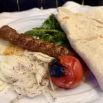 Adana Kebab s lavašem a grilovanou zeleninou na talíři v restauraci v Ankaře
