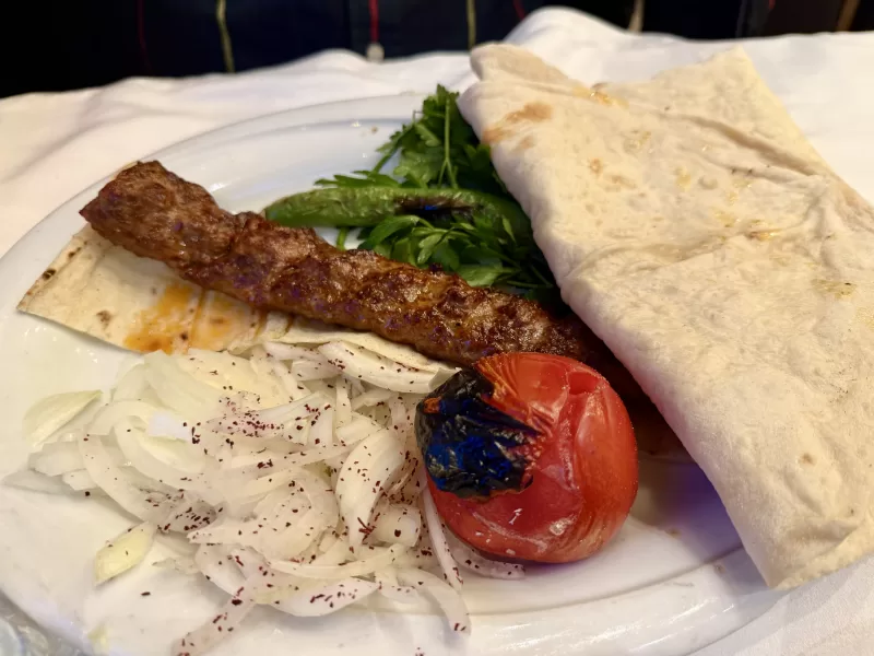 Adana Kebab s lavašem a grilovanou zeleninou na talíři v restauraci v Ankaře