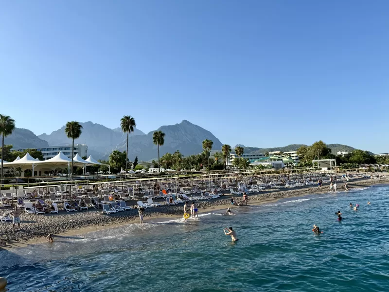 Výhled na moře, hory, palmy, v moři se koupají lidi